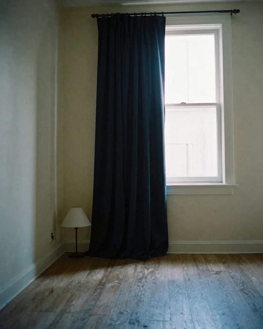 Dim bedroom at dusk with a blackout curtain partly drawn, a cool
