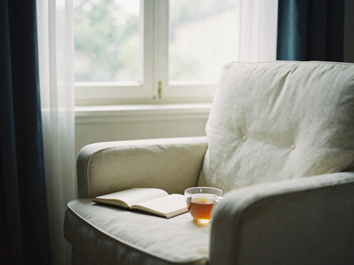 Soft window daylight on a quiet cream armchair beside an open not